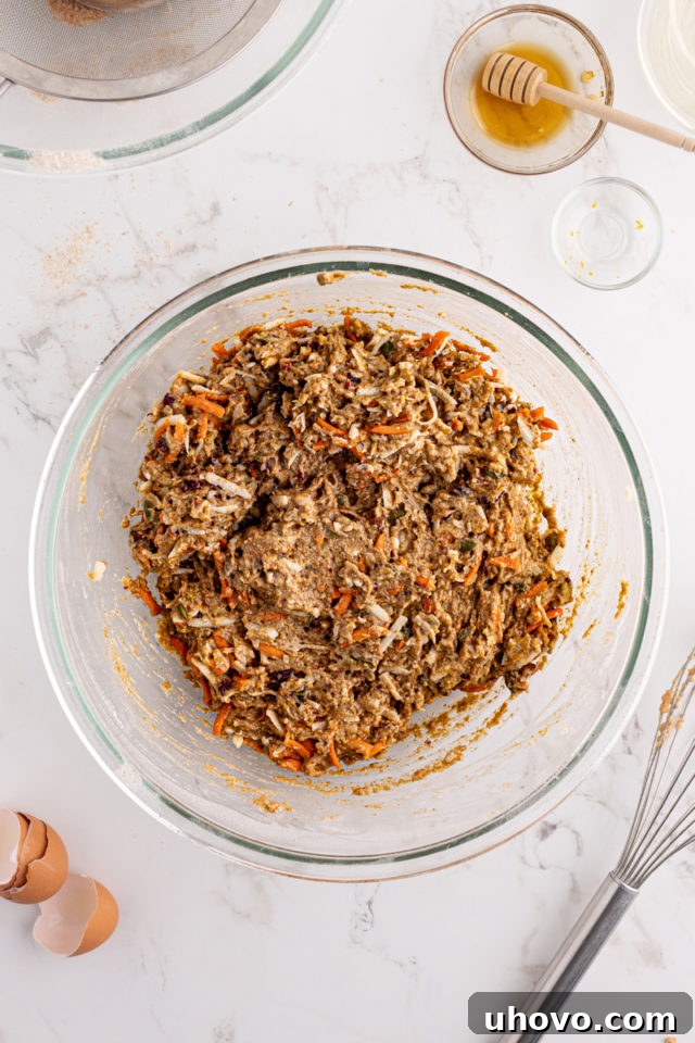 Overhead view of the fully mixed morning glory muffin batter in a glass bowl, showcasing a rich blend of fruits, vegetables, nuts, and seeds throughout.