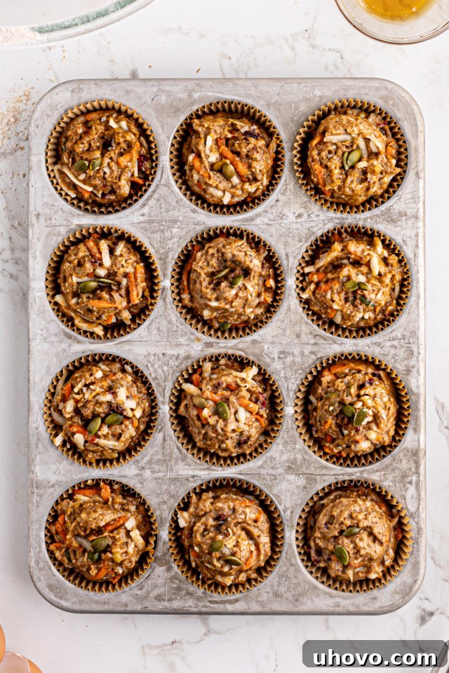 Overhead view of morning glory muffin batter neatly scooped into 12 muffin cups in a muffin pan, ready for baking.