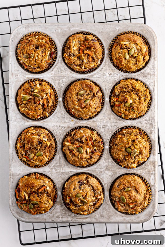 Overhead view of freshly baked Morning Glory Muffins, golden brown and perfectly domed, cooling in a muffin pan on a wire rack.