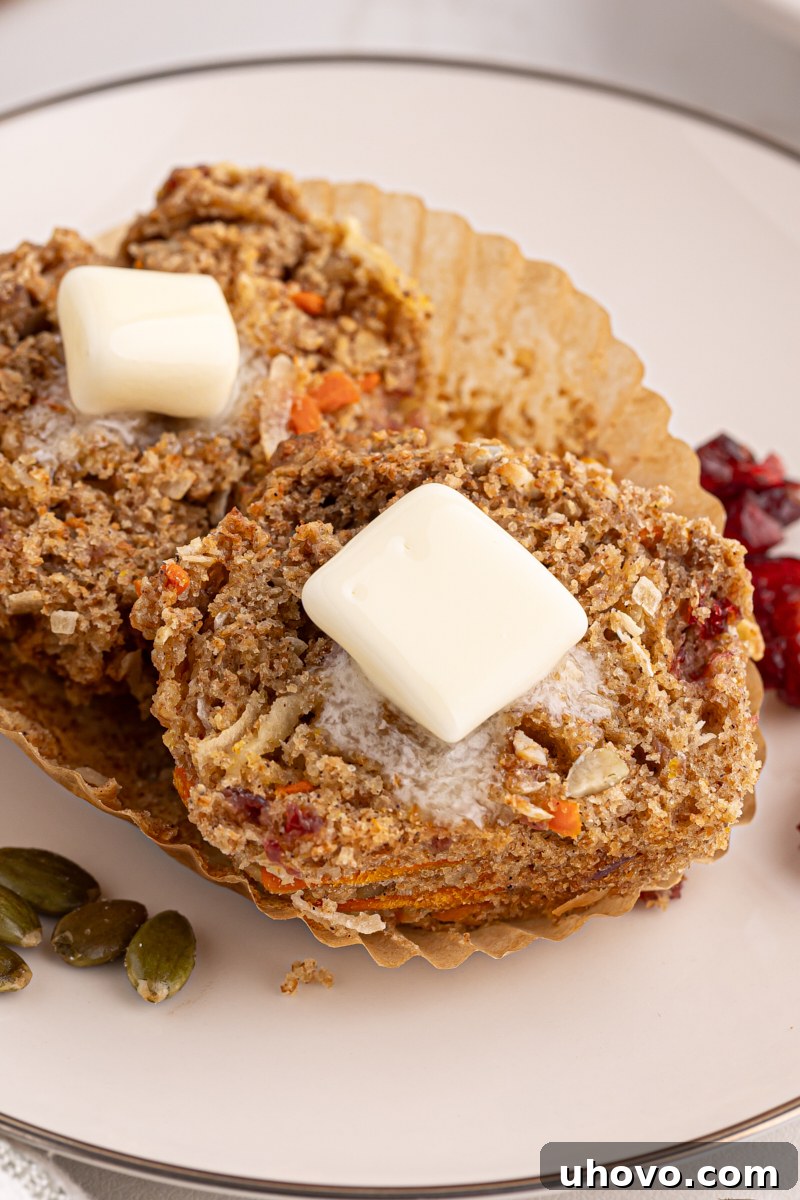 A Morning Glory Muffin split in half, revealing its moist interior and rich mix of ingredients, topped with a melting pat of butter, inviting a delicious bite.