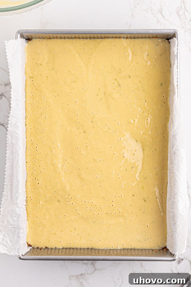 The vibrant green key lime pie filling being poured evenly over the baked graham cracker crust in a baking pan.