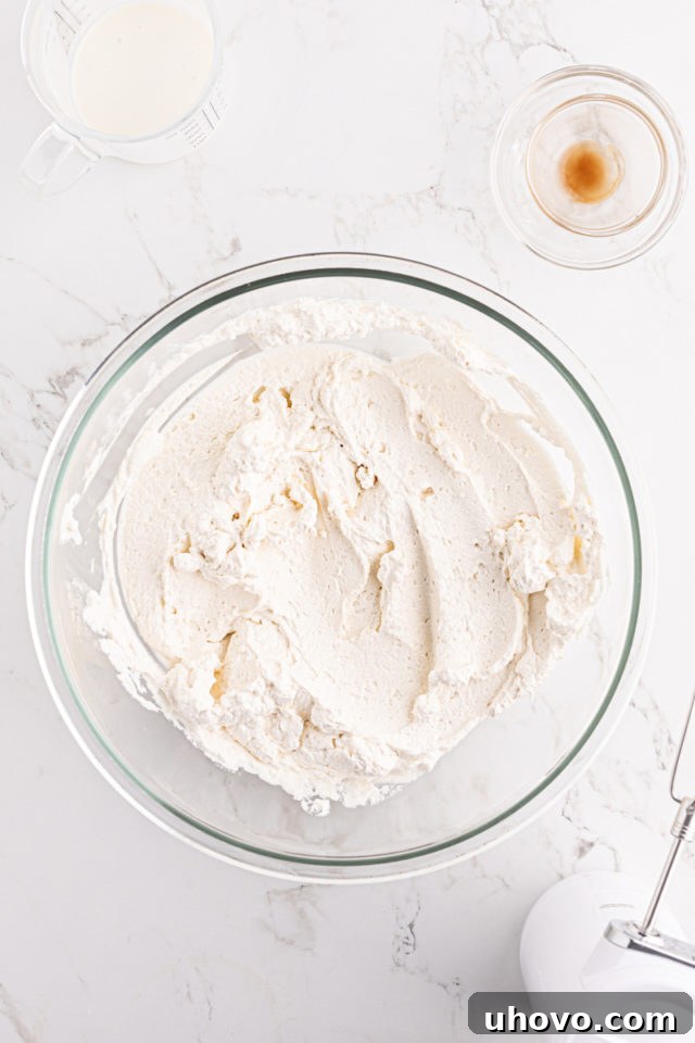 A glass mixing bowl filled with freshly whipped cream, showing perfect stiff peaks, indicating it's ready for topping.