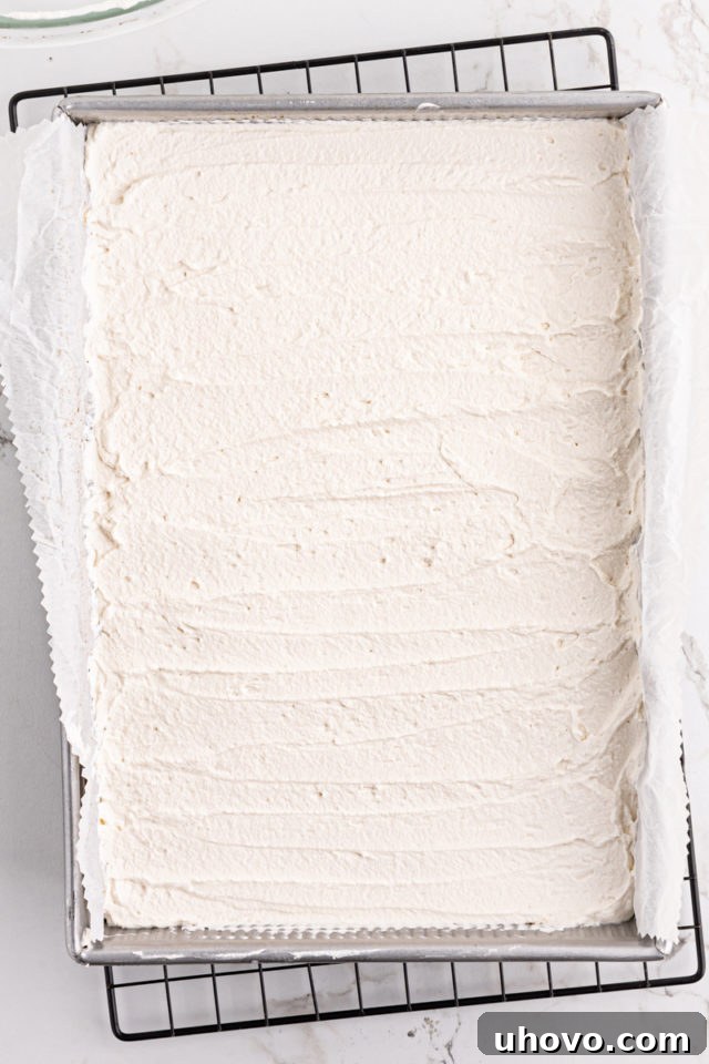 The key lime pie bars topped with a generous, evenly spread layer of fresh whipped cream, ready for chilling.