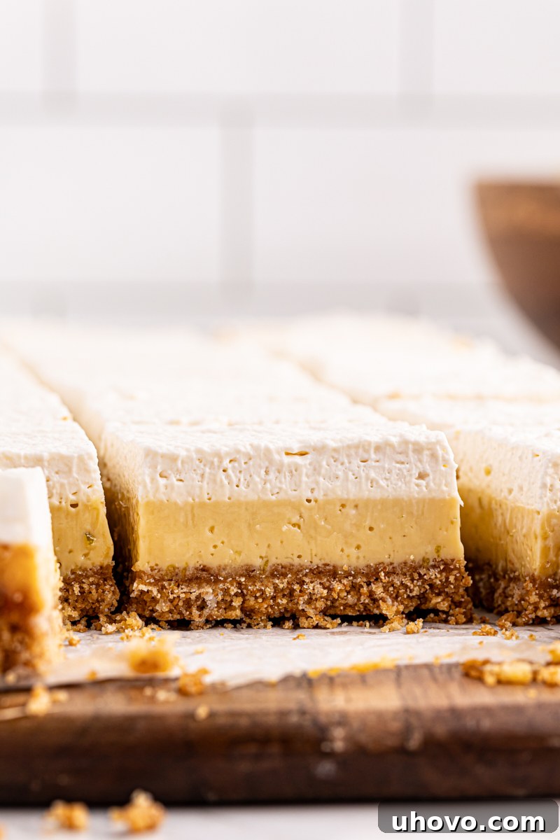 A cutting board filled with perfectly sliced key lime pie bars, showcasing their distinct layers of crust, filling, and whipped cream.