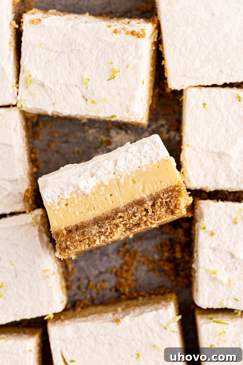 An overhead view of several perfectly sliced key lime pie bars on a wooden cutting board, with one bar turned on its side to display the distinct layers.