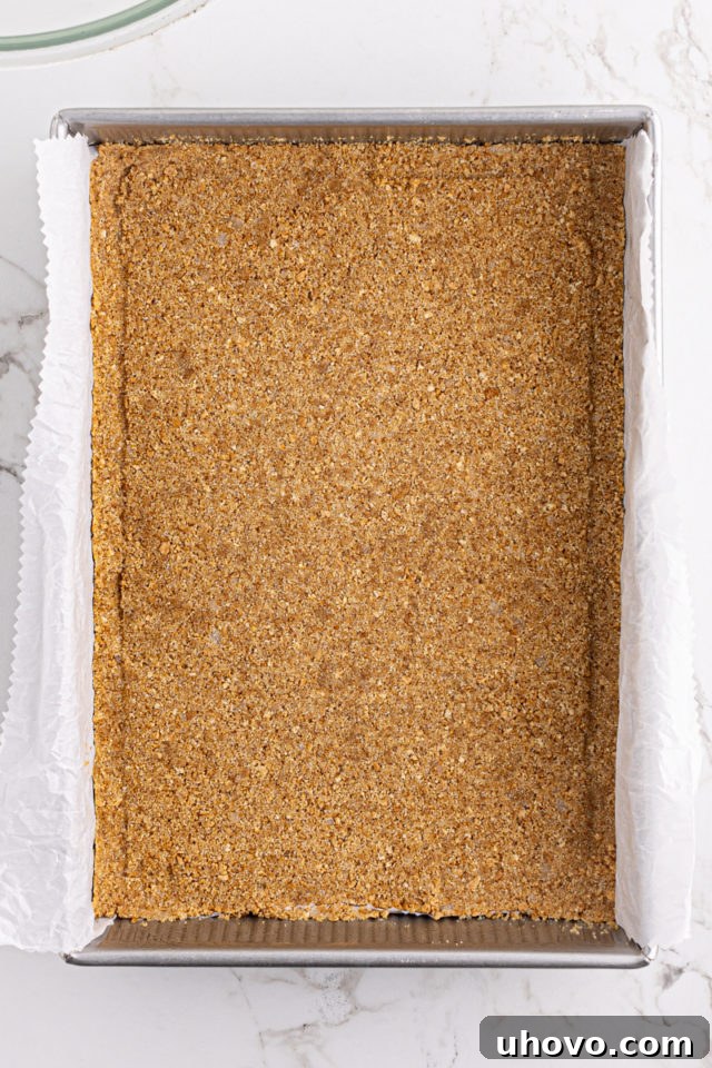 A perfectly pressed graham cracker crust lining the bottom of a 9x13 inch baking pan, ready for baking.