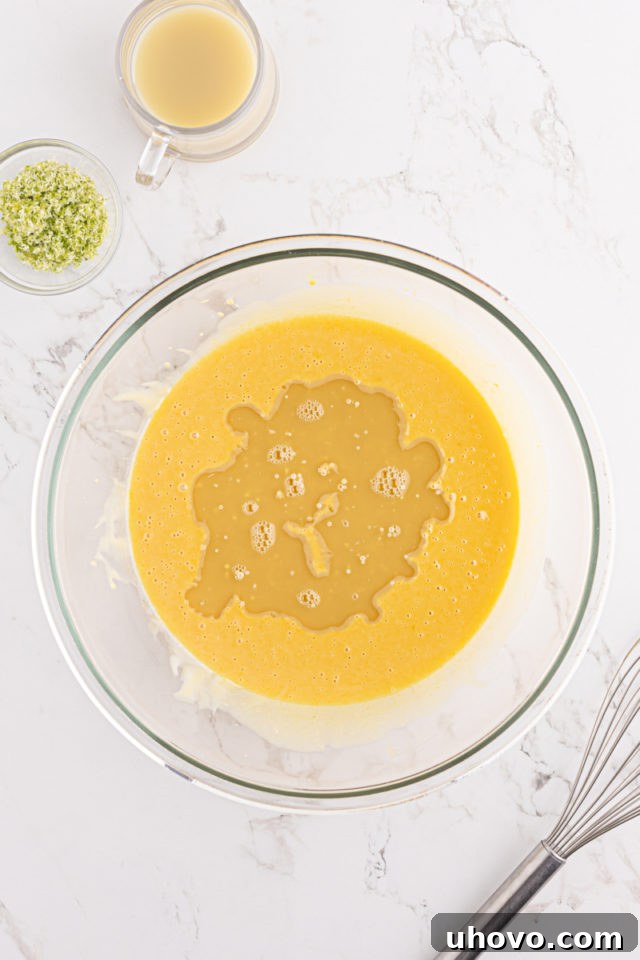 Key lime juice being poured into the mixture of sweetened condensed milk and egg yolks in a glass bowl, creating a vibrant yellow-green hue.