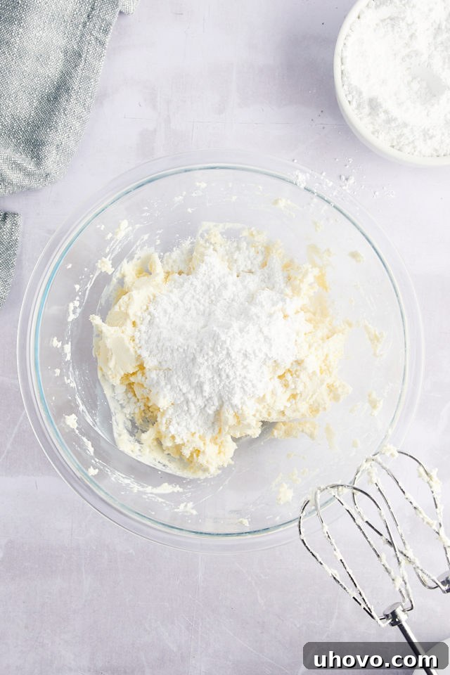 Overhead view of powdered sugar added to cream cheese mixture in bowl
