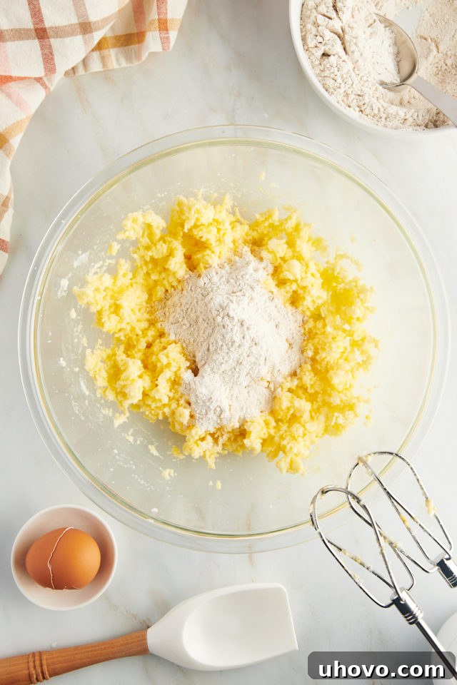 Overhead view of dry ingredients, a flour and spice mixture, being gradually added to the creamed butter and sugar in a large mixing bowl.