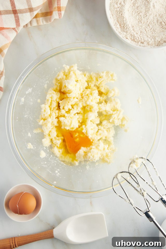 Overhead view of a cracked egg being added to a bowl of creamed butter and sugar, showing the light and fluffy texture.