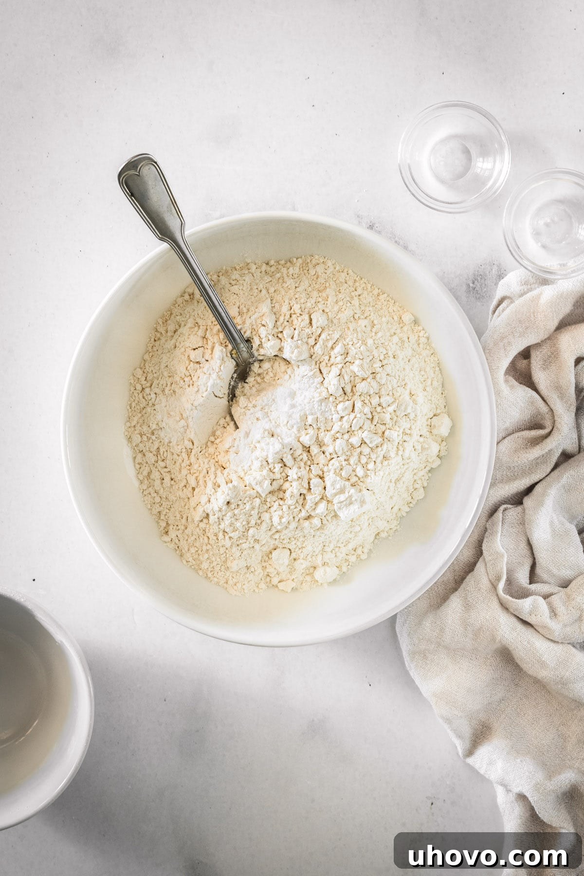 Overhead view of the dry ingredients for the cake, including flour, baking powder, baking soda, and salt, mixed in a bowl with a spoon.