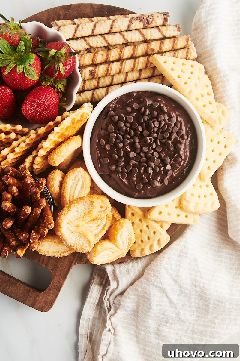 An overhead shot of a delightful brownie batter dip and a wide variety of dippers artfully arranged on a rustic round wooden board.