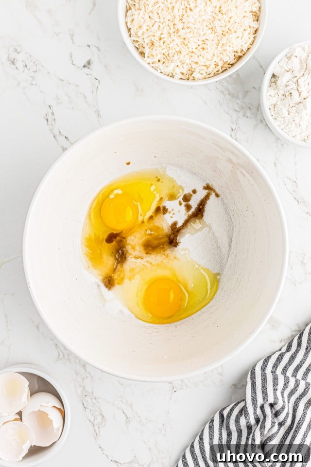 Overhead view of eggs, sugar, and vanilla extract being whisked together for the gooey coconut topping