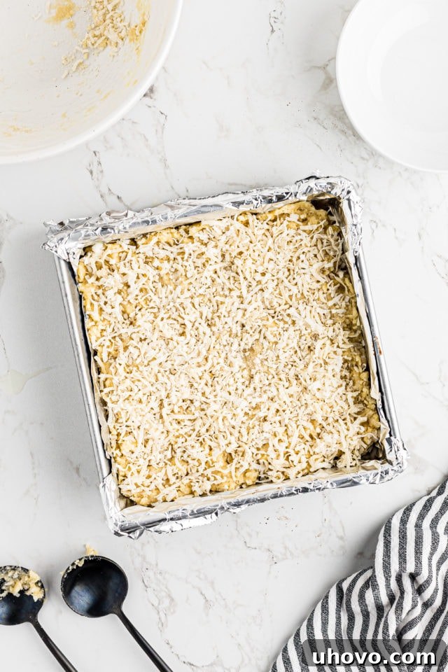 Overhead view of unbaked black bottom coconut bars with extra shredded coconut sprinkled on top for a finishing touch