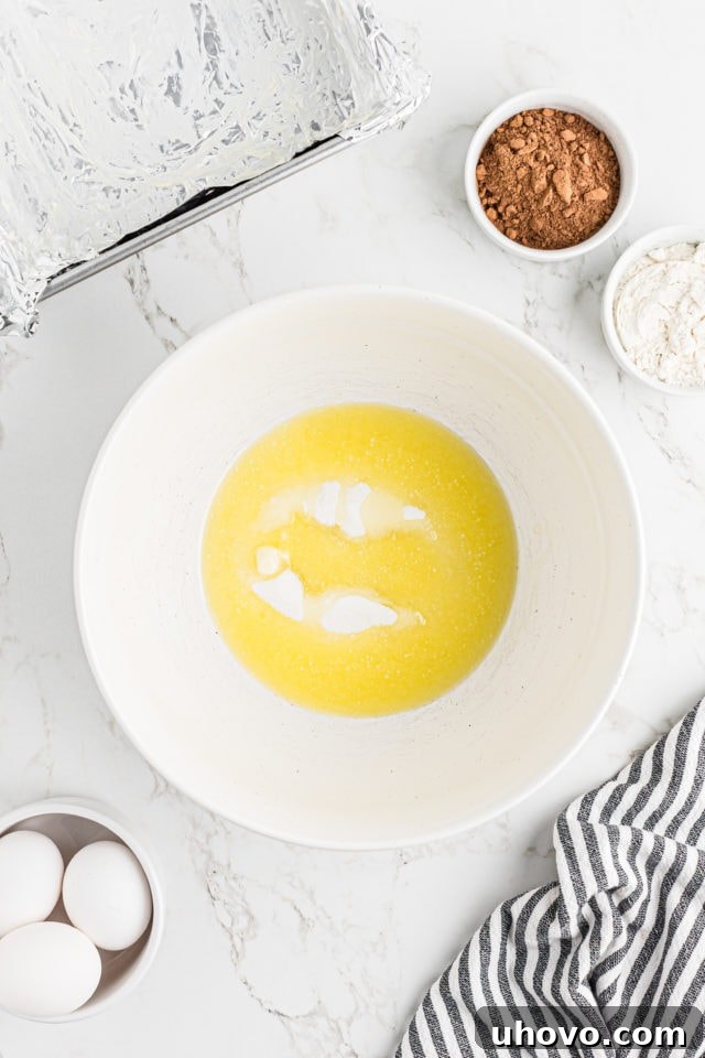 Overhead view of melted butter, granulated sugar, and salt being mixed in a bowl for the brownie crust