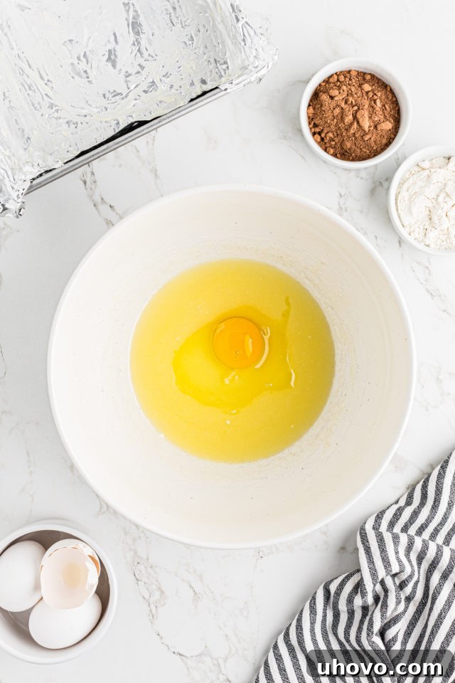 Overhead view of a single egg being added to the melted butter, sugar, and salt mixture for the brownie base