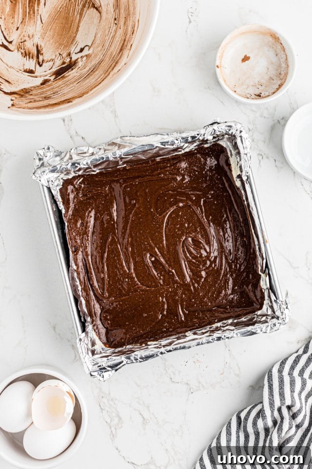 Overhead view of the rich brownie batter spread evenly in a foil-lined baking pan