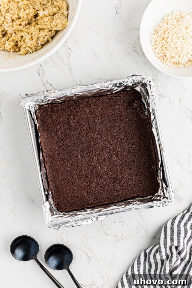 Overhead view of the baked brownie bottom layer in the pan, slightly pulled away from the edges