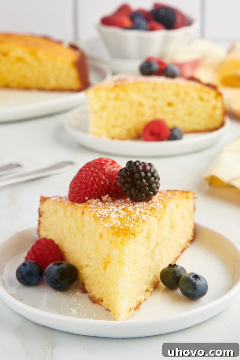 a slice of lemon ricotta cake served with fresh berries on a white plate, showcasing its moist texture and golden crust