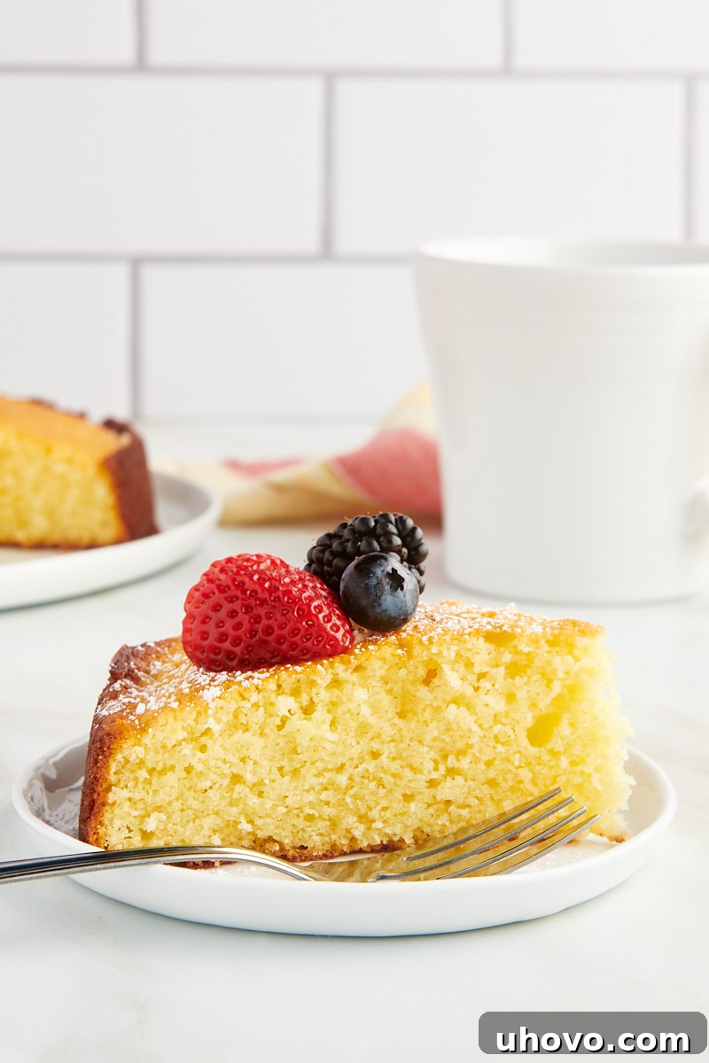 a beautifully presented slice of lemon ricotta cake, generously topped with an assortment of fresh berries, served on a crisp white plate