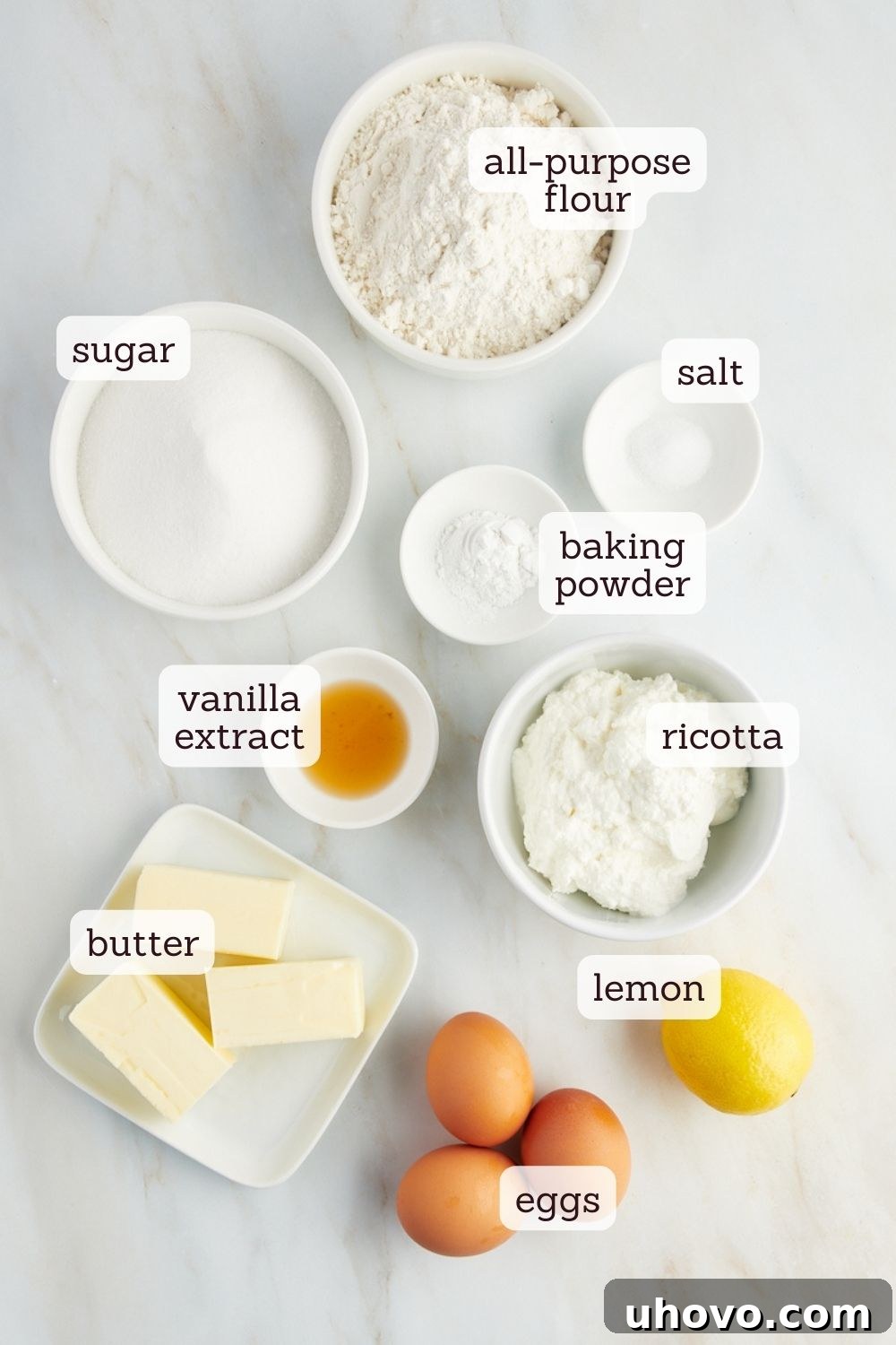 overhead view of fresh ingredients for lemon ricotta cake, including flour, sugar, butter, eggs, and a lemon