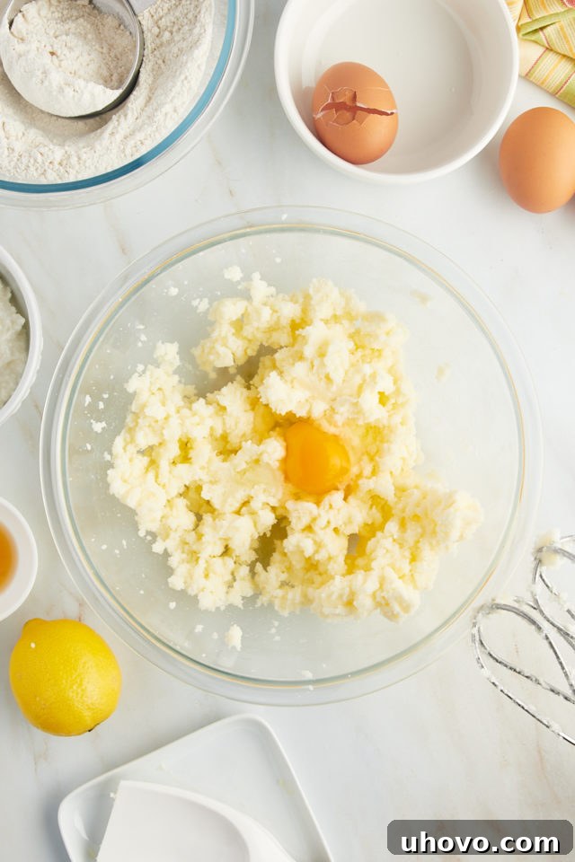 overhead view of an egg being added to the creamed butter and sugar mixture in a glass mixing bowl, ready for mixing