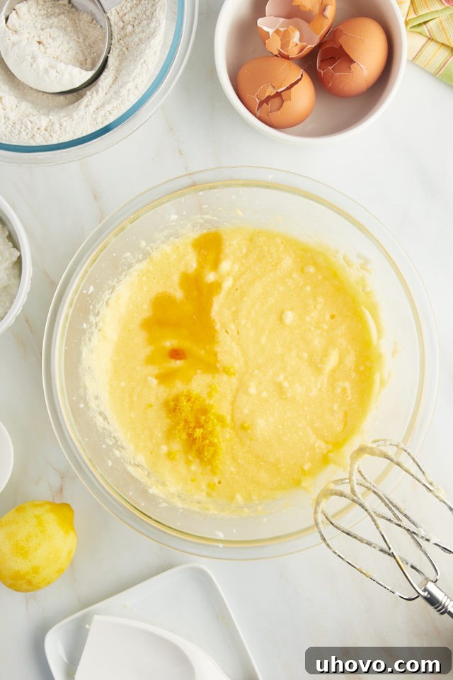 overhead view of vanilla extract and vibrant lemon zest being added to the partially mixed ricotta cake batter in a glass bowl