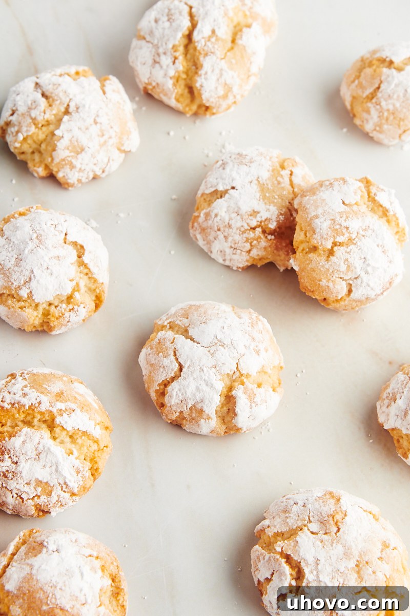 Overhead view of perfectly baked Amaretti cookies arranged on a kitchen countertop, showcasing their signature cracked tops and golden edges.