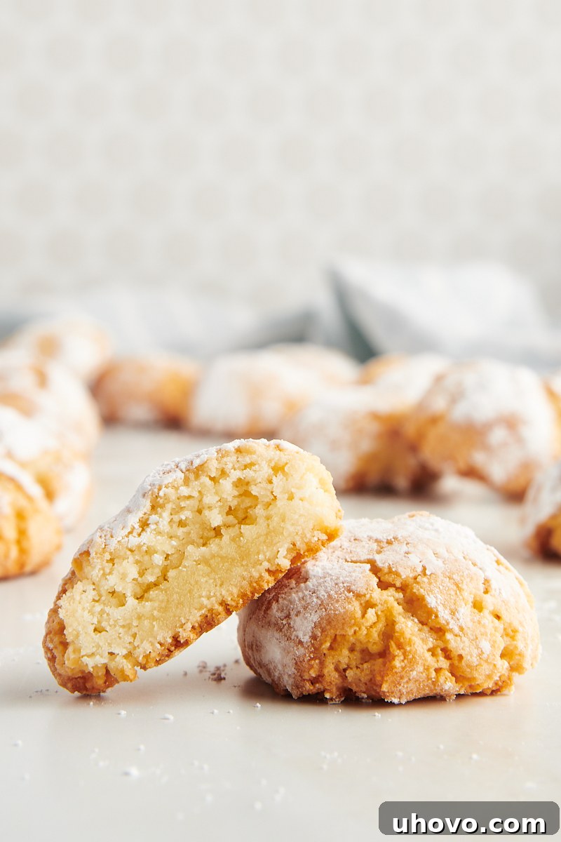 Two Amaretti cookies stacked on a plate, with one cut in half to clearly display its wonderfully chewy and moist interior texture, highlighting the perfect bake.