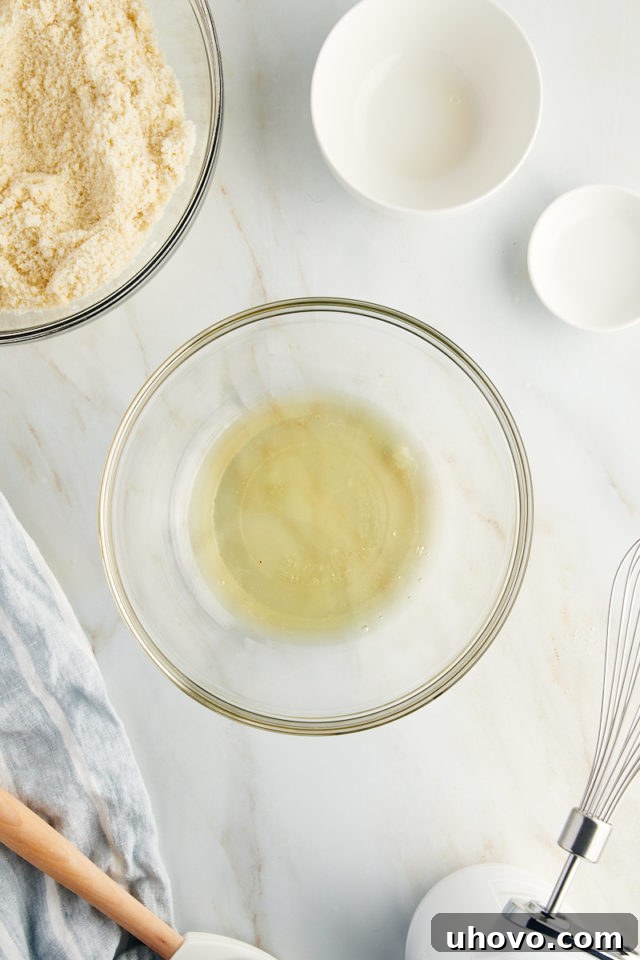 Overhead view of two egg whites in a glass bowl, showcasing their room temperature state before beating for Amaretti cookies.