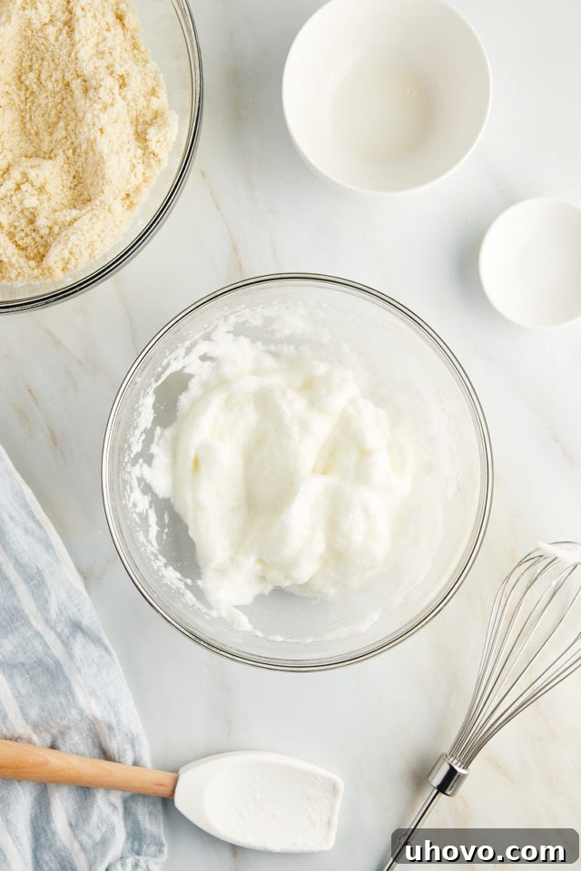 Overhead view of beaten egg whites in a bowl after almond extract has been added and gently folded in, preparing them for the cookie dough.