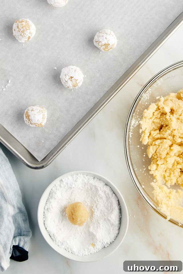 Overhead view showing the process of rolling a ball of Amaretti cookie dough in confectioners' sugar to coat it evenly before baking.