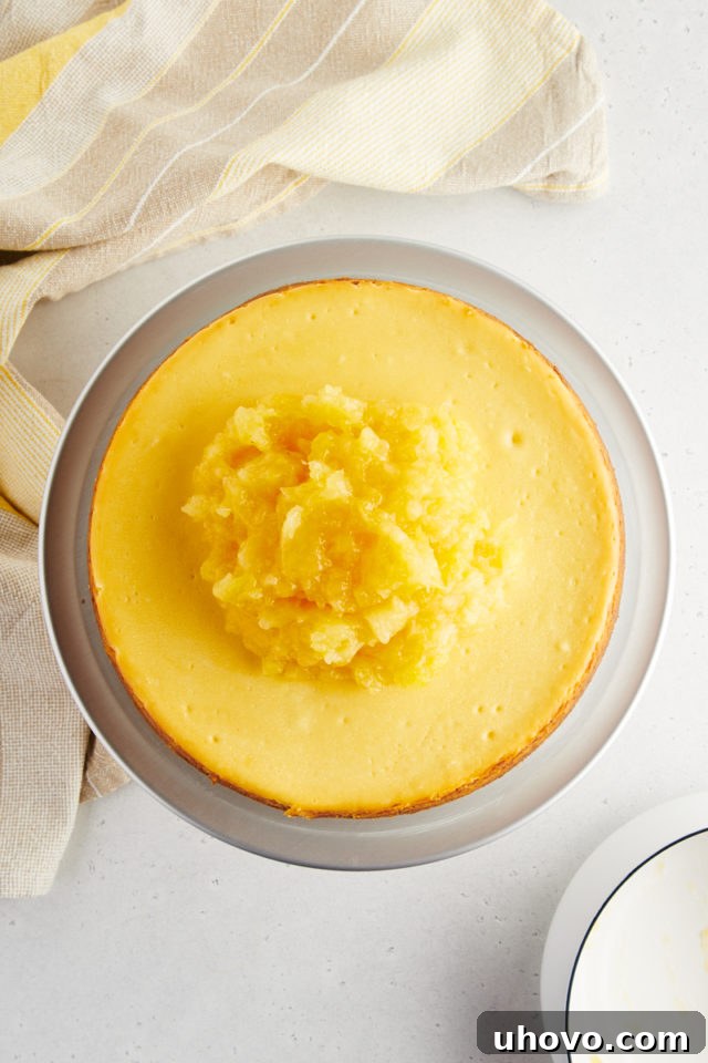 An overhead shot of the completed pineapple topping, glistening and spread generously over the chilled, whole cheesecake, creating a vibrant and inviting surface.