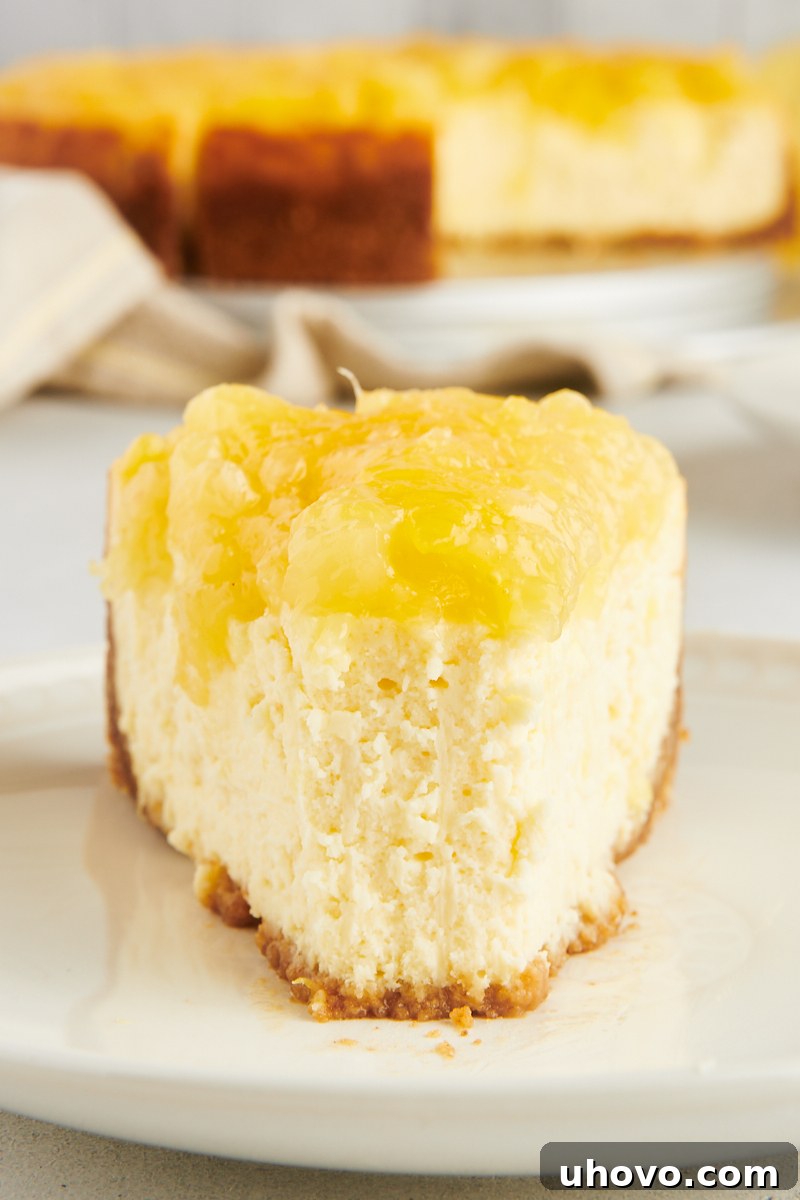 A close-up, head-on view of a single slice of pineapple cheesecake on a plate, with a small bite taken from the tip, highlighting its creamy texture and the sweet pineapple topping.