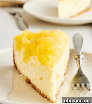 Head-on view of pineapple cheesecake slice on plate, showcasing its perfect layers and vibrant topping.