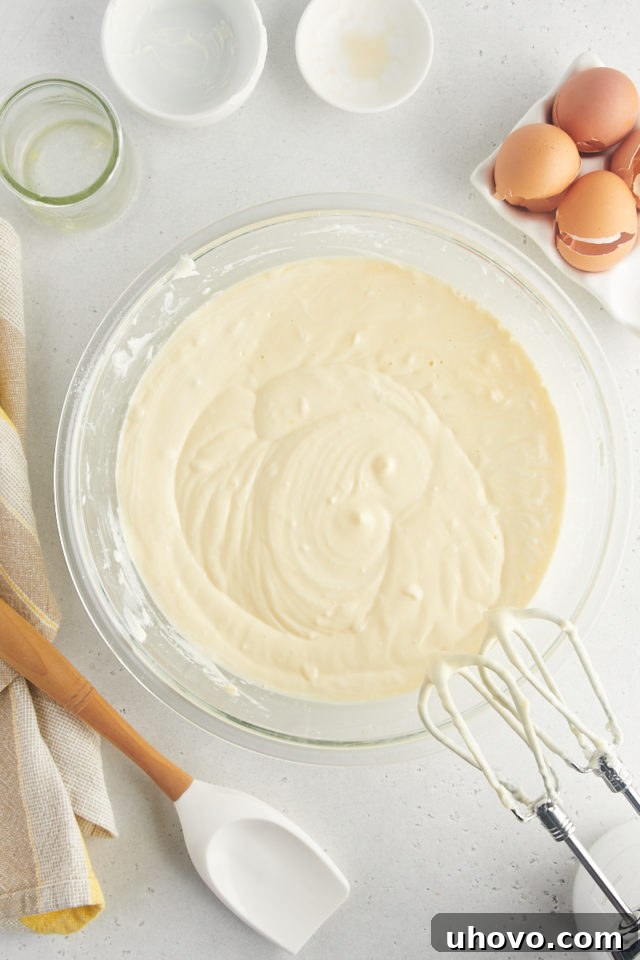 An overhead view of the creamy, pale yellow cheesecake filling, smooth and perfectly blended in a large mixing bowl, showcasing its readiness for baking.