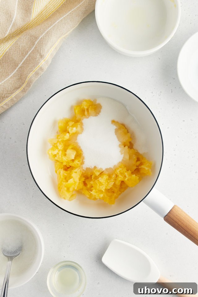 An overhead view of crushed pineapple mixed with sugar, simmering gently in a saucepan on the stovetop, illustrating the initial step in preparing the vibrant topping.