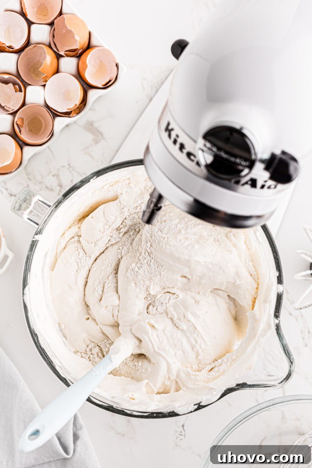Sifted flour and sugar mixture being carefully folded into the whipped egg whites, emphasizing delicate incorporation.