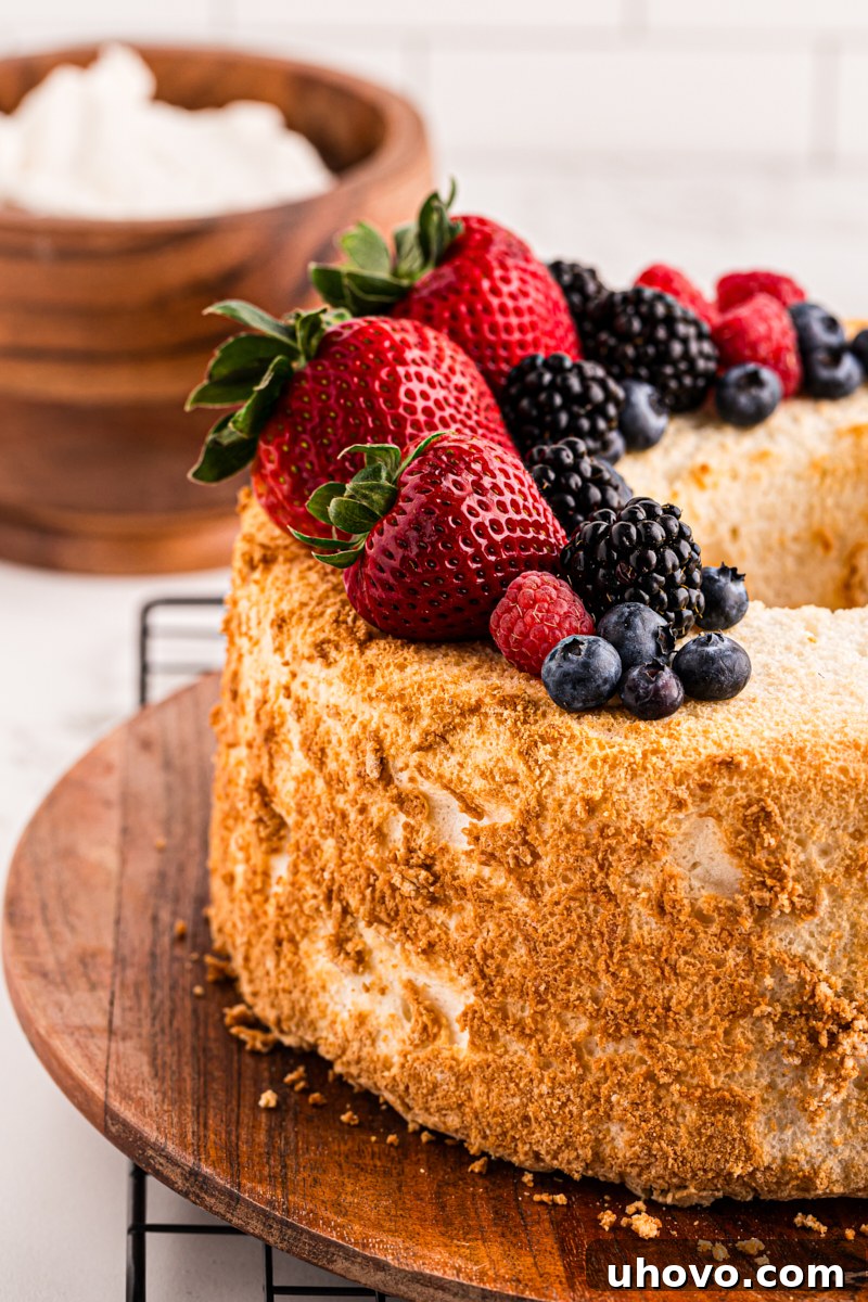 A perfectly baked Angel Food Cake adorned with fresh berries, with a side bowl of creamy whipped cream, ready for a delightful dessert experience.