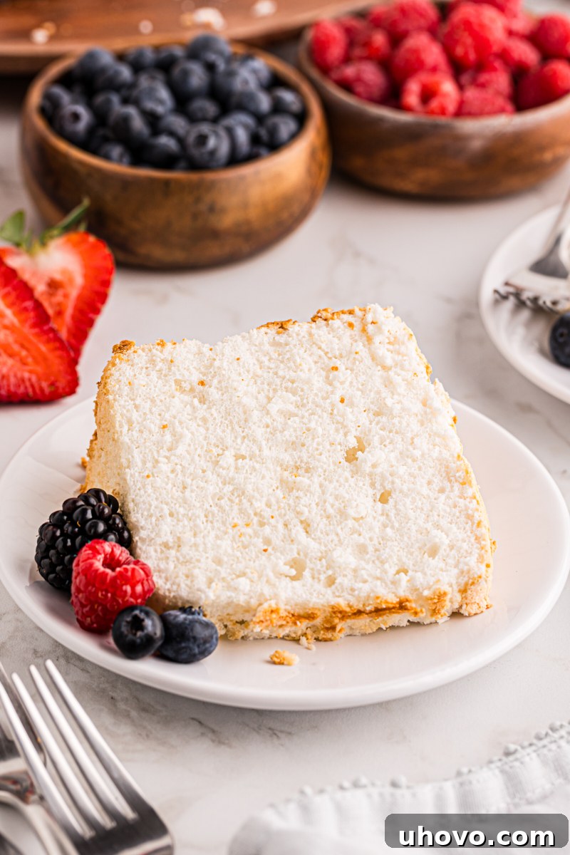 A pristine slice of Angel Food Cake elegantly presented on a white plate, accompanied by a vibrant scattering of fresh berries.
