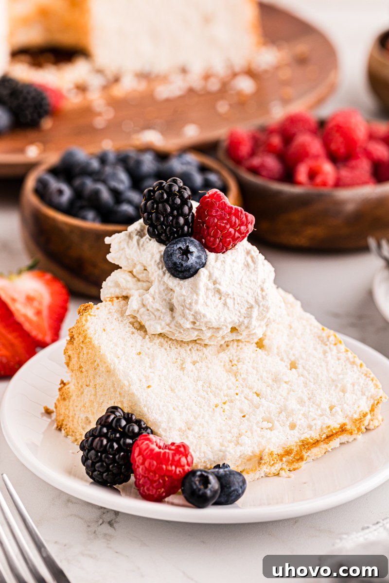 A delicate slice of Angel Food Cake crowned with fluffy whipped cream and a colorful assortment of fresh berries, ready to be enjoyed.