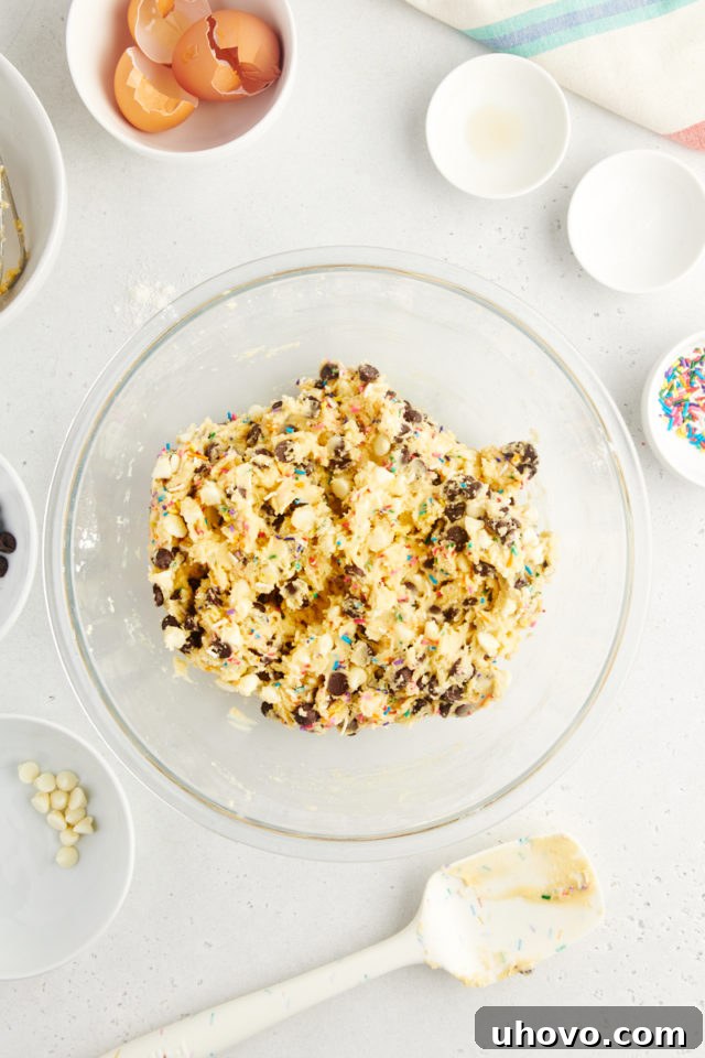 A close-up overhead view of the perfectly mixed sprinkle chocolate chip cookie dough in a glass bowl, uniform in color and consistency after all ingredients, including sprinkles and chocolate chips, have been combined.