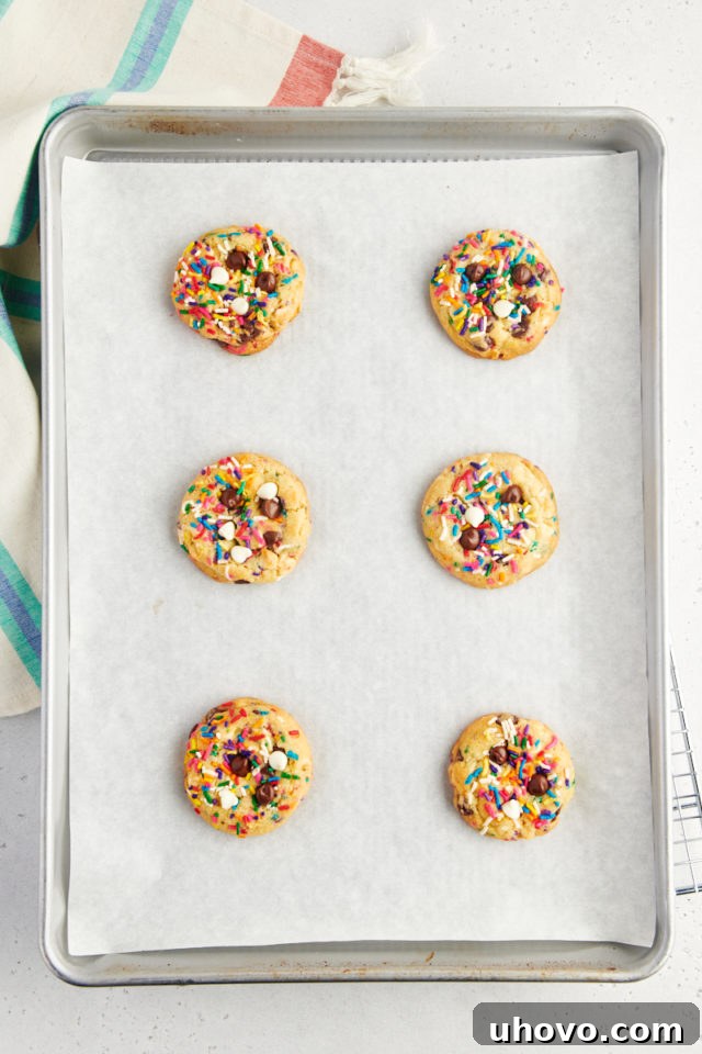 A parchment-lined baking sheet filled with freshly baked sprinkle chocolate chip cookies, their edges a beautiful golden brown and centers slightly soft, indicating perfect readiness.