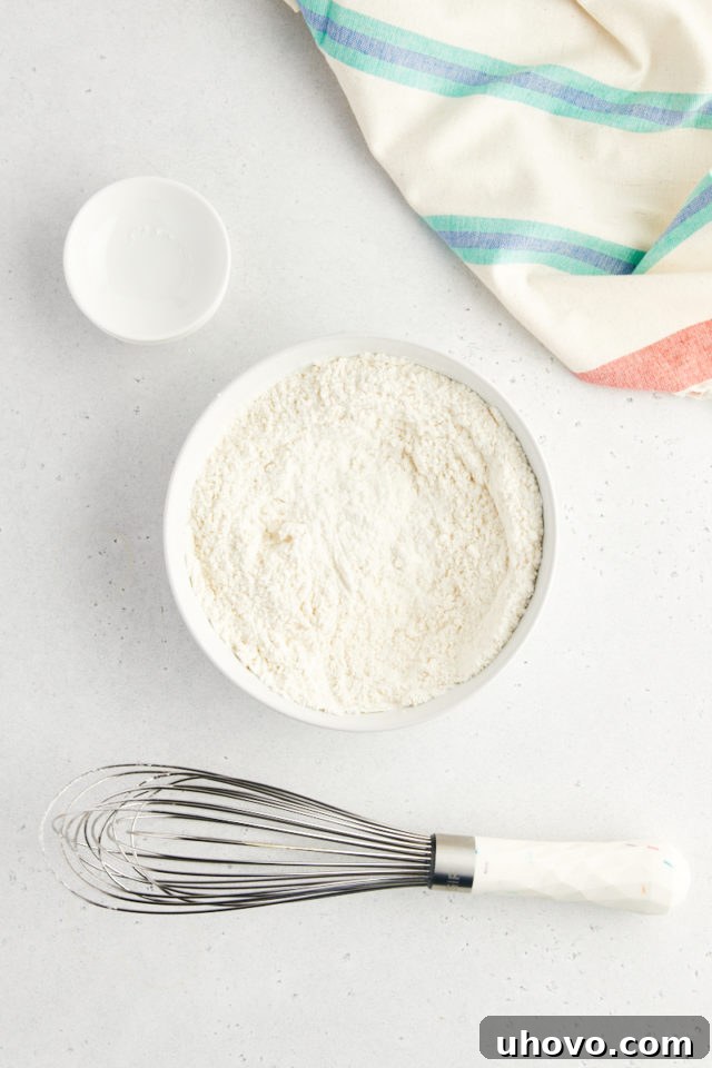 An overhead view of a glass mixing bowl containing white flour, cornstarch, baking soda, and salt, freshly whisked together to create a uniform dry ingredient mixture for sprinkle chocolate chip cookies.