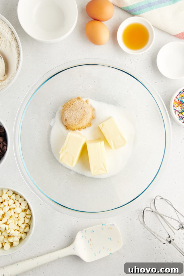A vibrant overhead view of softened unsalted butter, granulated sugar, and light brown sugar combined in a clear glass mixing bowl, having just been creamed together to a light and fluffy consistency.