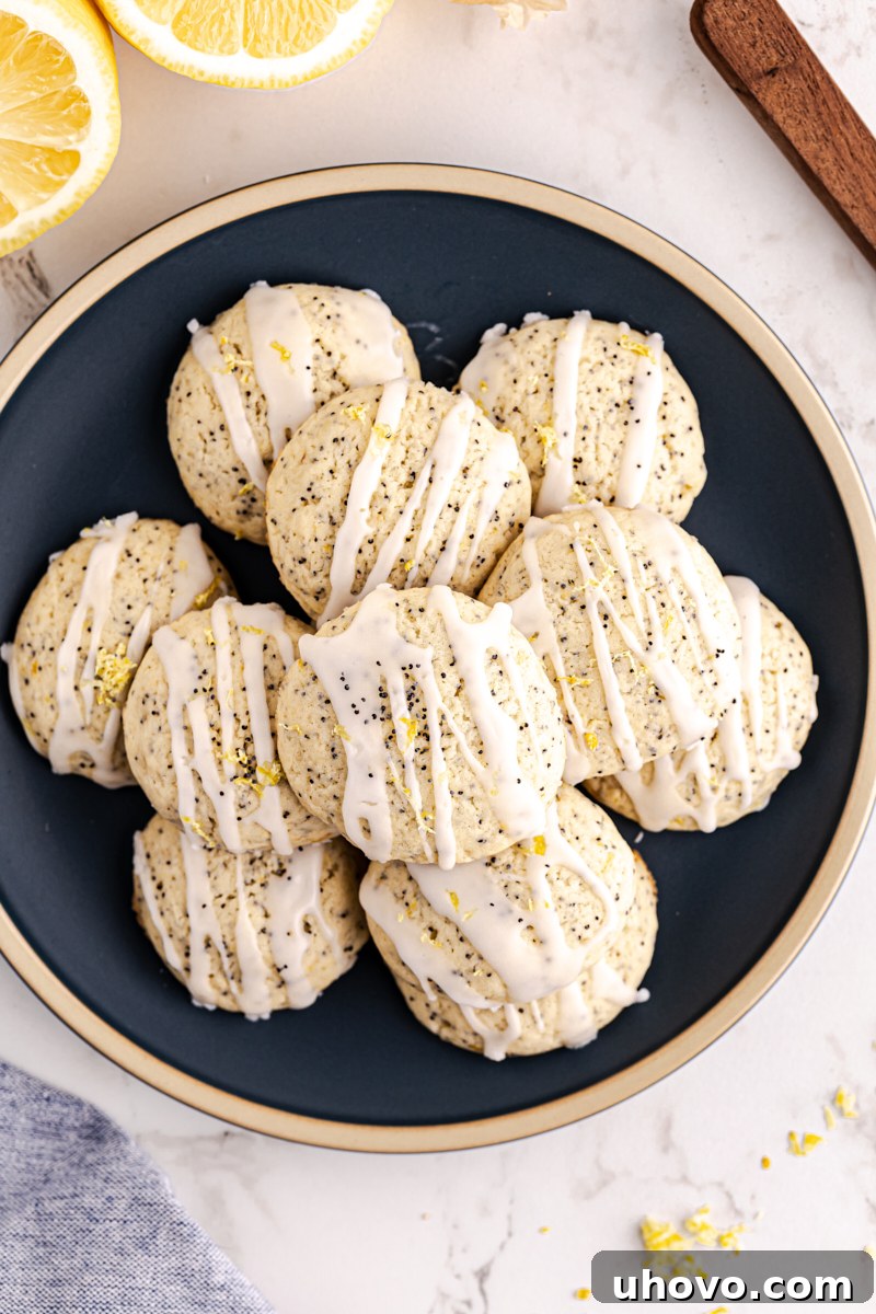 Overhead view of a stack of glazed lemon poppy seed cookies artfully arranged on a dark blue plate, ready to be served.