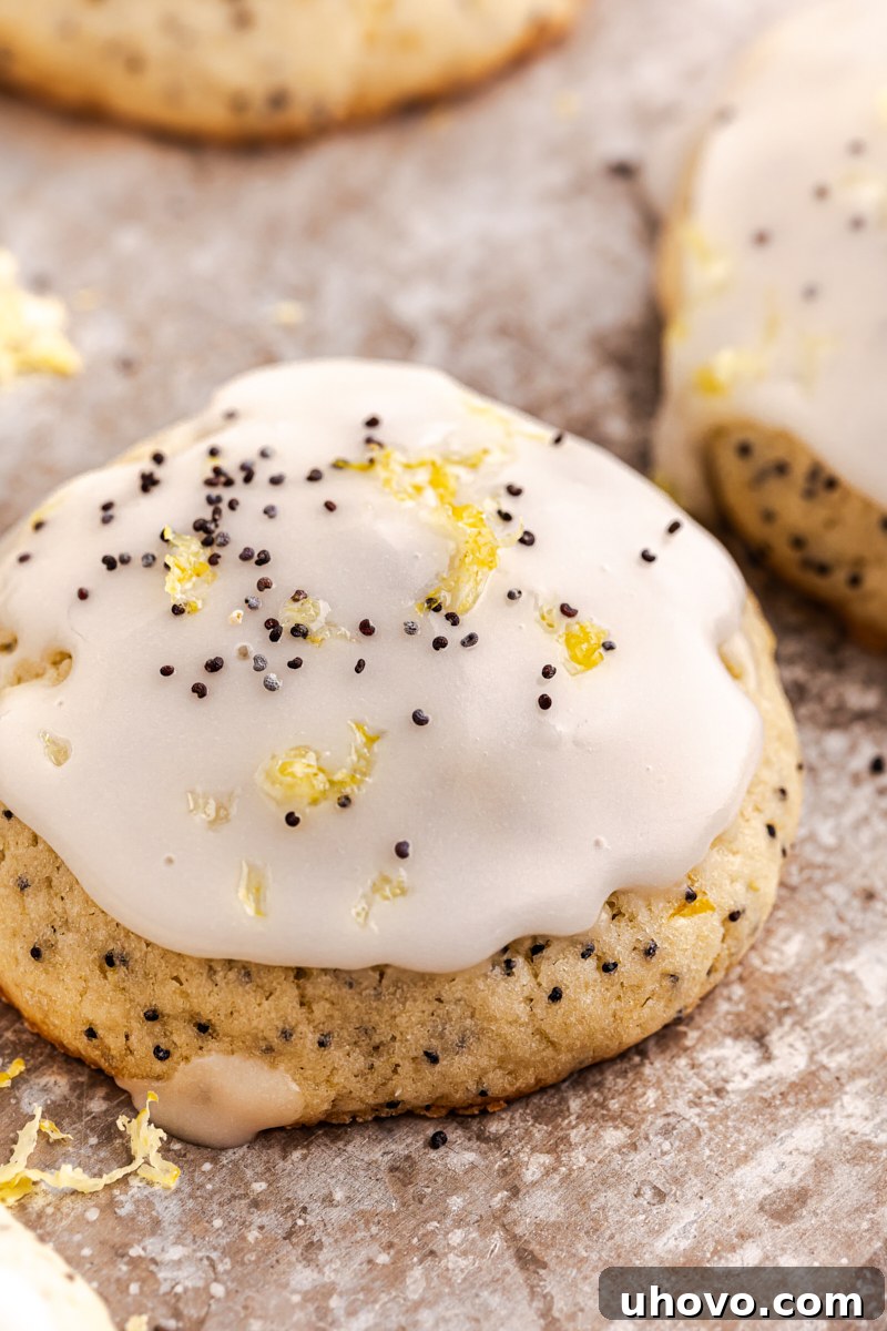 Close-up of a single lemon poppy seed cookie, generously topped with lemon glaze, sprinkled with fresh lemon zest, and a few poppy seeds, showcasing its appealing texture and garnish.