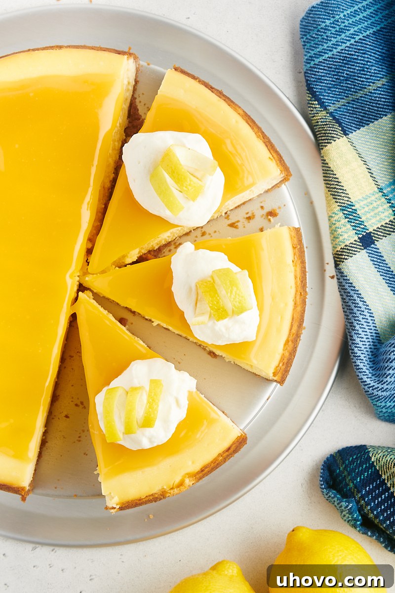 Overhead view of a partially sliced lemon cheesecake, beautifully adorned with lemon curd, delicate whipped cream, and elegant lemon curls.