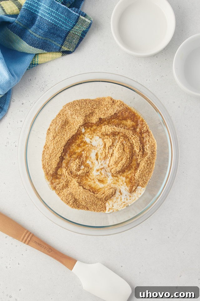 Overhead view of graham cracker crumbs, sugar, and melted butter in a glass mixing bowl, ready to be combined for the crust.