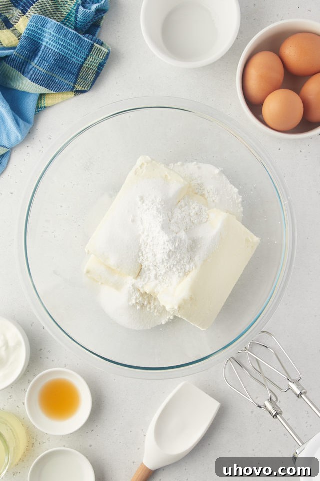 Overhead view of cream cheese, granulated sugar, and cornstarch in a glass mixing bowl, ready for blending.